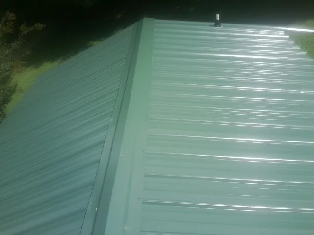 New green metal panels meeting at the ridge of a roof — Flat Roof Repair work by our crew in Maynardville