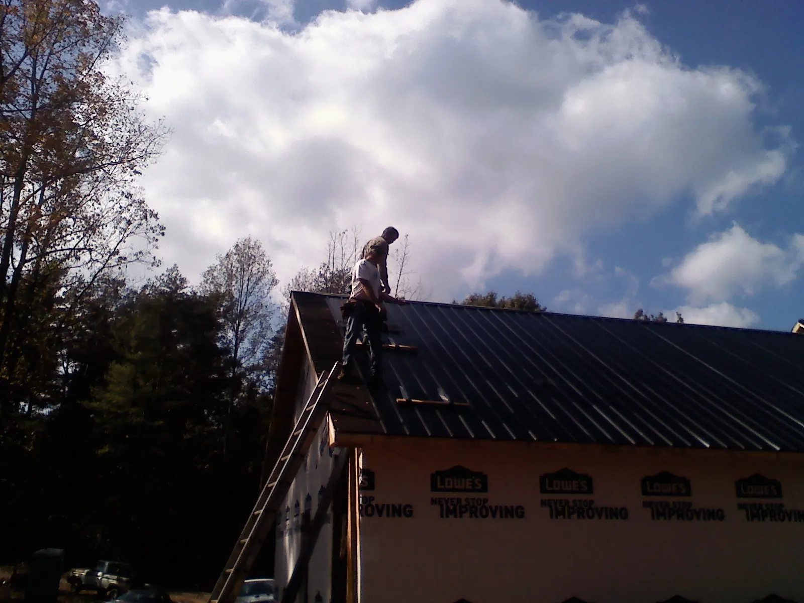 Roofer fastening dark metal panels high against a cloudy sky, from a Roof Inspection job in Maynardville