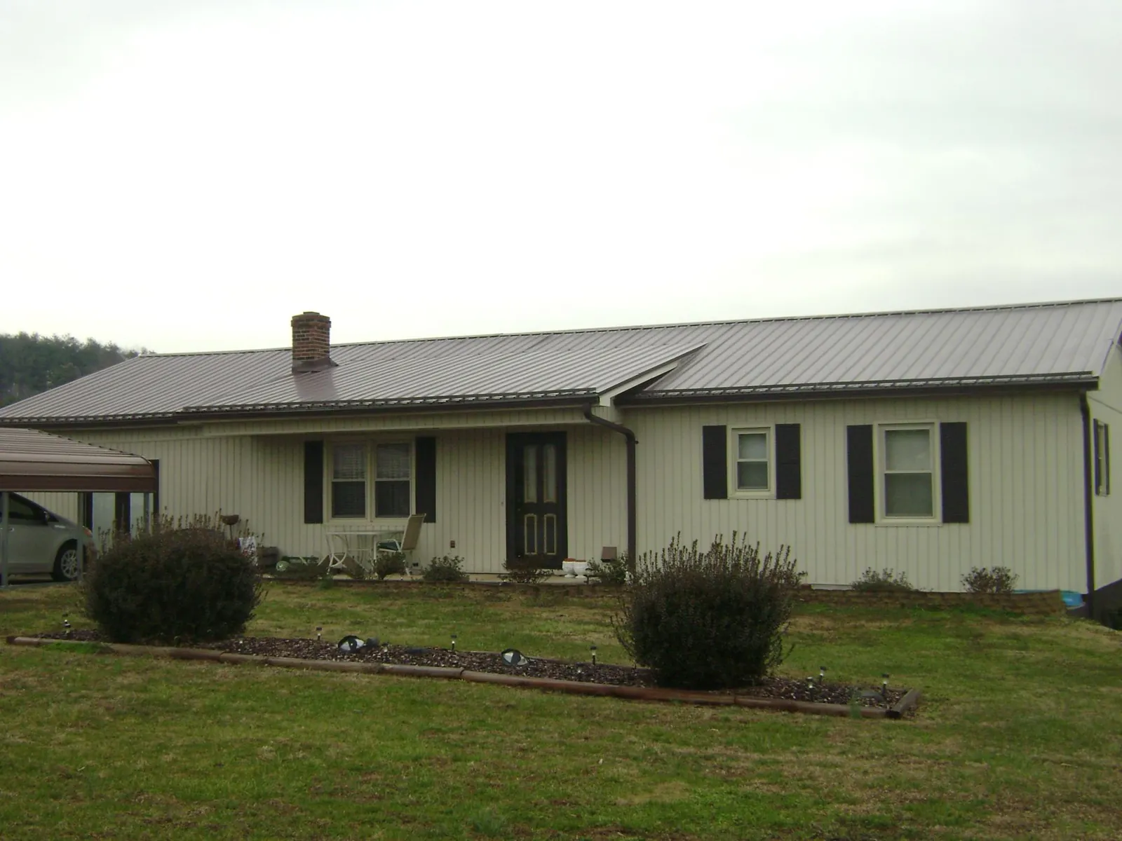 Brown metal roof on a cream sided ranch home with a brick chimney in Maynardville